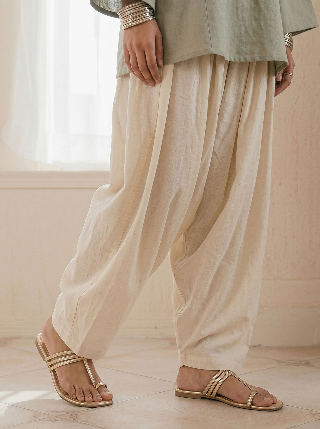 Off-white linen shalwar trousers with pleated drape and tan flat sandals