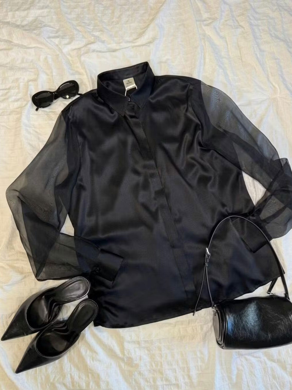 Black satin silk blouse laid flat, sheer organza sleeves and button placket